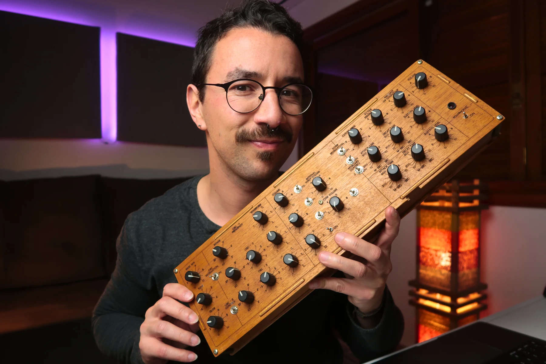 Gustavo Silveira no estúdio, segurando seu controlador MIDI de madeira